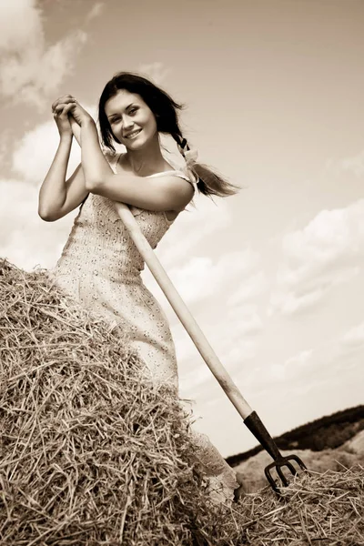 Joven morena sonriente en vestido de pie con horquilla de heno en las manos — Foto de Stock