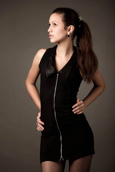 Modelo de mujer joven en mini vestido negro y medias de red de pesca de pie sobre fondo gris — Foto de Stock