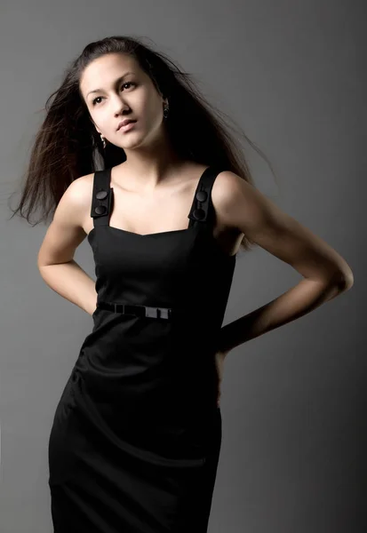 Modelo de mujer joven en vestido de noche negro de pie sobre fondo gris — Foto de Stock