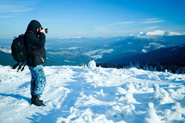 Photographer standing with camera on hill with panoramic view of winter valley