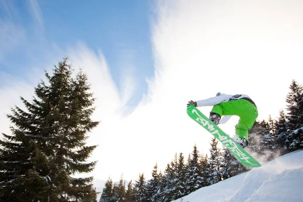 Giovane in abbigliamento sportivo che salta durante lo snowboard invernale — Foto Stock