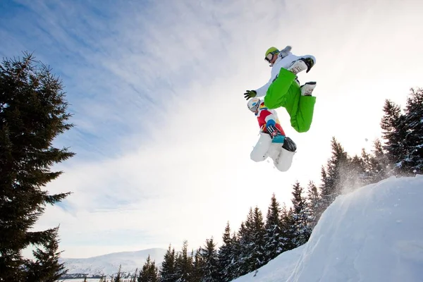 Junger Mann in Sportkleidung beim Snowboarden über Kiefern — Stockfoto