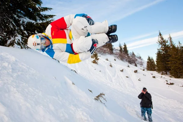 Fotografo che fotografa il giovane in abbigliamento sportivo che salta durante lo snowboard — Foto Stock