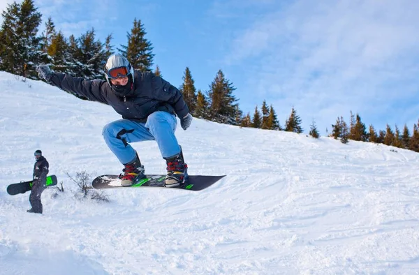 Giovane uomo in abbigliamento sportivo snowboard su sfondo pini — Foto Stock