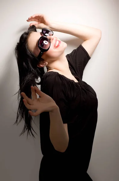 Young brunette woman in black dress and glasses standing and smiling — Stock Photo, Image