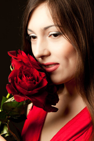 Portrait of young woman model in red dress holding red rose flower in hand