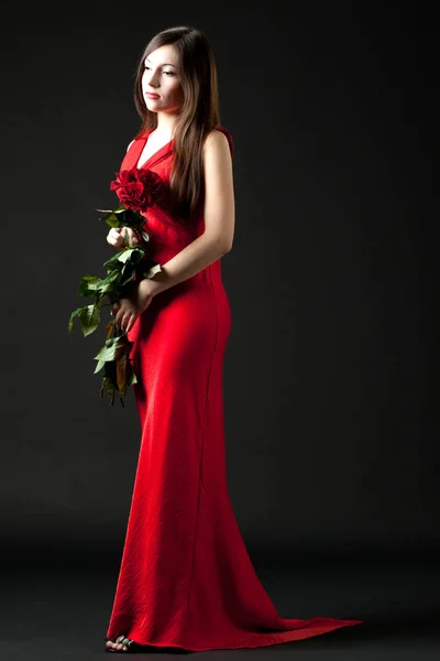 Modelo de mujer joven en vestido rojo de pie y con ramo de rosas rojas — Foto de Stock