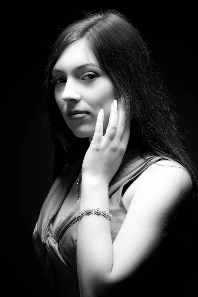 Black and white portrait, young woman model in cocktail dress standing over dark background in photo studio. Beauty and fashion concept