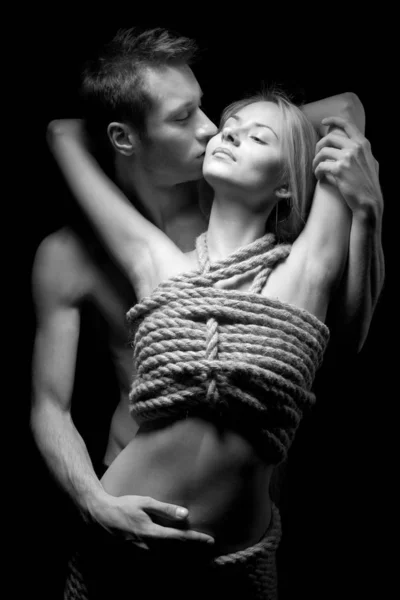 Мужчина обнимает и целует свою женщину обнаженным телом, покрытым веревками — стоковое фото