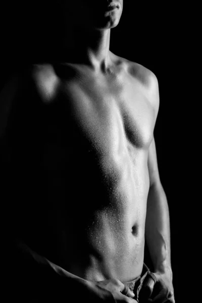 Young athletic man with naked torso in jeans standing over black background