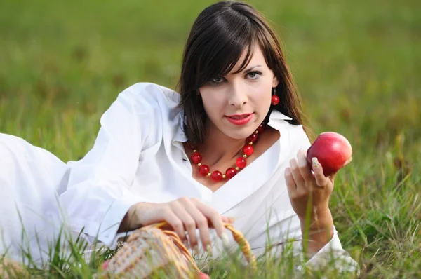 A lány a fűben fekszik és almát tart a kezében. — Stock Fotó