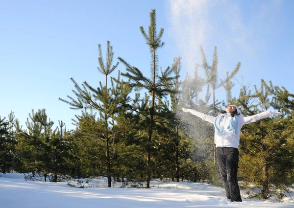 Woman stands among pine trees and throws up snow — 스톡 사진