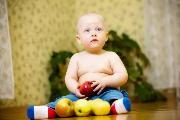 Child sits on floor and holds apple in his hands — 스톡 사진