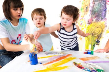 Kadın ve bebekler masada otururken resim çiziyorlar.