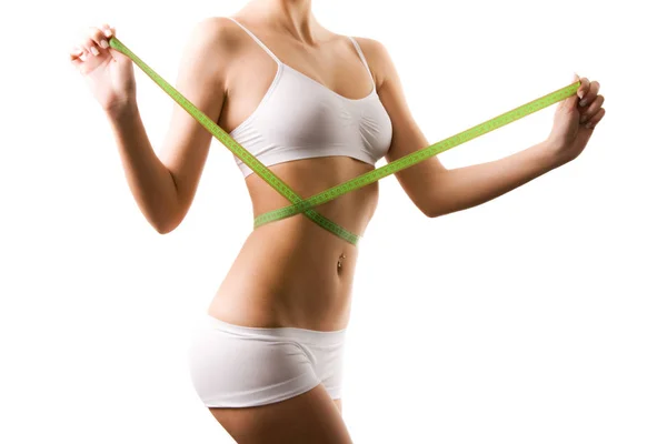 Body of young woman in white shorts and top measuring waist with tape measure in hands over white background — Stock Photo, Image