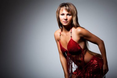 Genç, zayıf, uzun saçlı, seksi kırmızı, parlak kostümlü, dans eden, siyah arka planda duran güzel bir kadın.