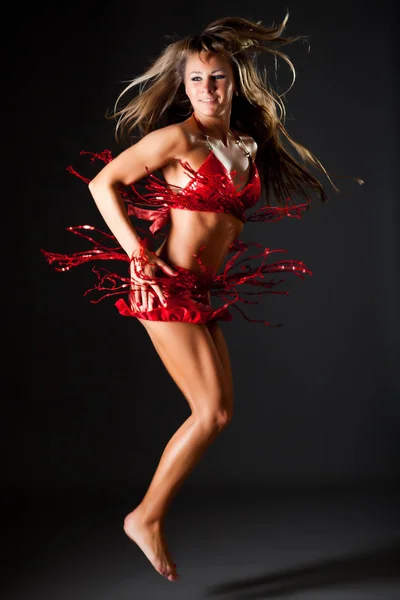 Jeune mince belle femme aux cheveux longs en costume rouge brillant sexy sautant sur fond sombre — Photo