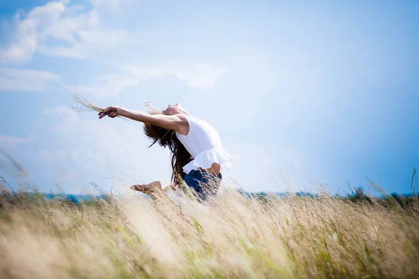 Jonge vrouw in casual kleding staan in rogge veld en genieten van de zon op de zomerdag met blauwe lucht op de achtergrond — Stockfoto