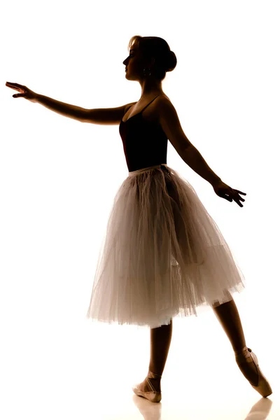 Silhueta de bailarina bonita jovem em tutu branco e sapatos pontiagudos fazendo dança pose — Fotografia de Stock