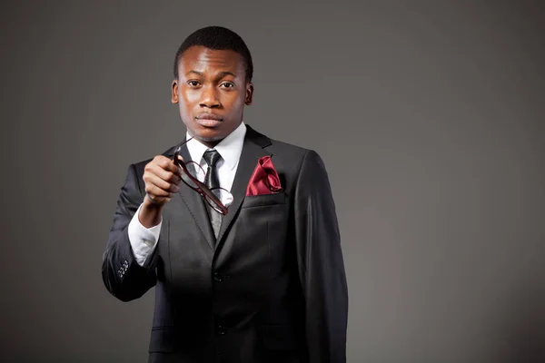 Joven hombre de negocios africano guapo en traje gris, camisa blanca, corbata y gafas de pie y sonriente —  Fotos de Stock