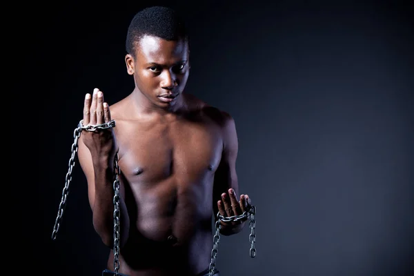 Joven hombre africano medio desnudo de pie y sosteniendo cadenas masivas en las manos —  Fotos de Stock