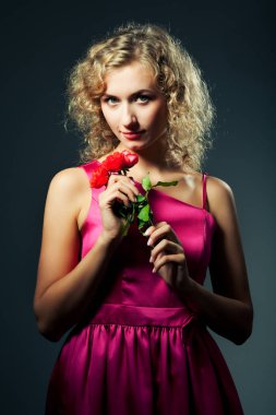 Genç, zayıf, sarışın, mor elbiseli, kıvırcık saçlı, gülümseyen ve kameraya bakan bir kadın.