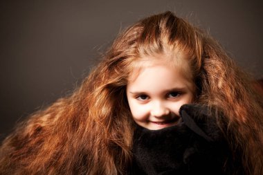 Koyu gri arka planda uzun kahverengi saçlı küçük pozitif kızın portresi.