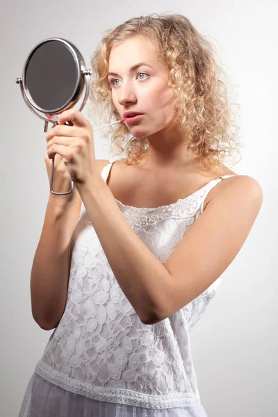 Joven mujer rubia delgada hermosa con el pelo rizado en blanco mini vestido sexy mirando pequeño espejo y sonriendo — Foto de Stock