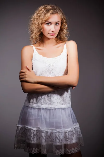 Jong slank mooi blond vrouw met krullend haar in wit sexy jurk staan en kijken naar camera over grijze achtergrond — Stockfoto