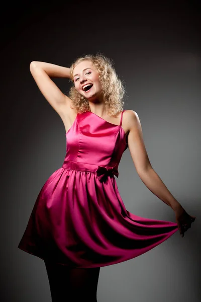 Молодая стройная красивая блондинка с вьющимися волосами в фиолетовом платье стоя, улыбаясь и глядя в камеру — стоковое фото