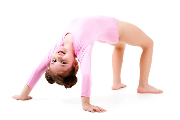 Pequeña chica positiva en traje de gimnasia rosa de pie en pose de puente y sonriendo sobre fondo blanco — Foto de Stock