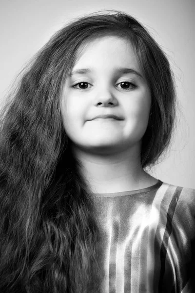 Retrato de pequena menina positiva com cabelos castanhos longos sobre fundo cinza escuro — Fotografia de Stock