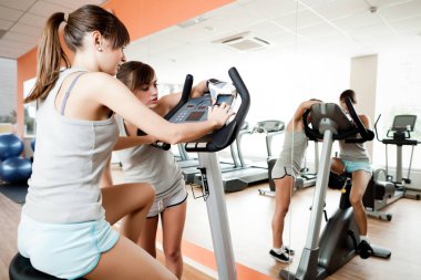 Spor giyim bölümünde genç ve güzel bir kadın spor salonunda spor aletini kullanması için başka bir kıza yardım ediyor.
