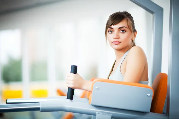 Jóvenes hermosas mujeres en ropa deportiva haciendo ejercicio utilizando la máquina de fitness para las piernas con gimnasio vacío en el fondo — Foto de Stock