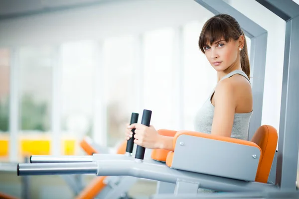 Jóvenes hermosas mujeres en ropa deportiva haciendo ejercicio utilizando la máquina de fitness para las piernas con gimnasio vacío en el fondo —  Fotos de Stock