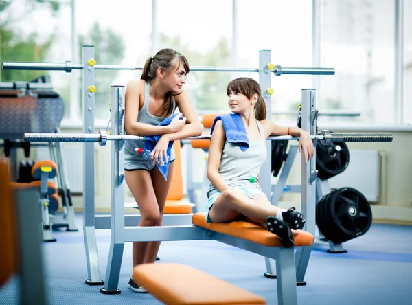 Deux jeunes belles femmes minces en vêtements de sport gris avec des serviettes avec bouteille d'eau et en se regardant dans la salle de gym — Photo