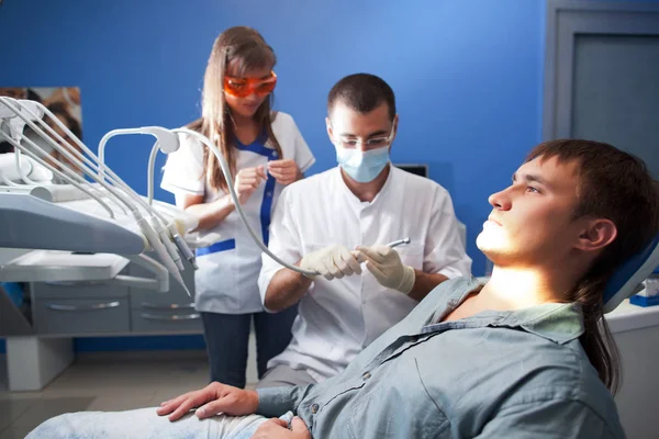 Jeune dentiste médecin homme en uniforme blanc et masque spécial et jeune infirmière femme examinant homme patient dans le cabinet dentaire — Photo