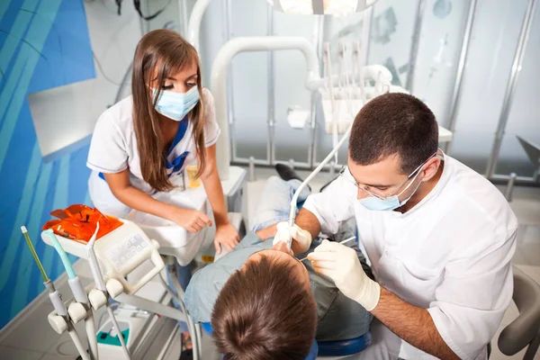 Jovem dentista médico homem em uniforme branco e máscara especial e jovem enfermeira mulher examinando homem paciente em consultório odontológico — Fotografia de Stock