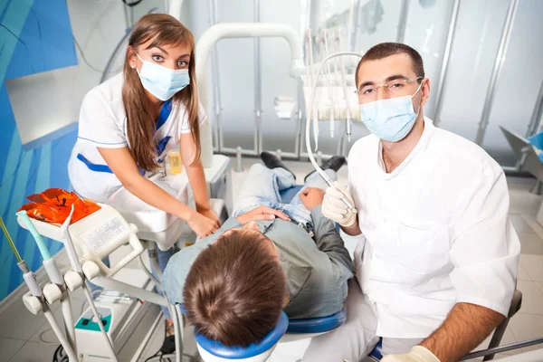 Jovem dentista médico homem em uniforme branco e máscara especial e jovem enfermeira mulher examinando homem paciente em consultório odontológico — Fotografia de Stock
