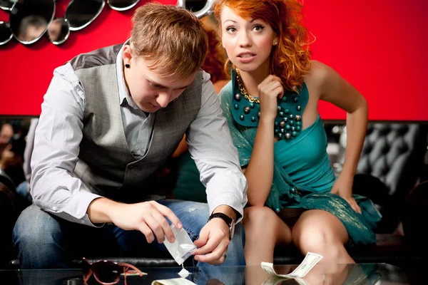 Young couple in cocktail wear sitting and ready to use drugs in powder from small package Royalty Free Stock Photos