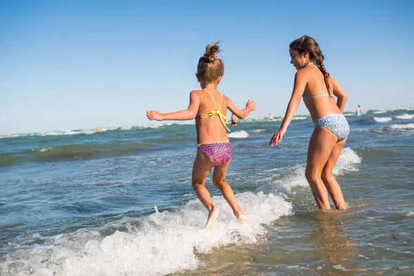 Dos niñas divertidas saltan en las ruidosas olas del mar —  Fotos de Stock