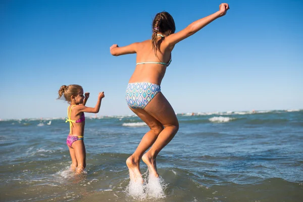 Deux petites filles drôles sautent dans les vagues bruyantes de la mer — Photo