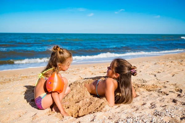 Petite fille joyeuse enterrer sa sœur aînée dans le sable — Photo