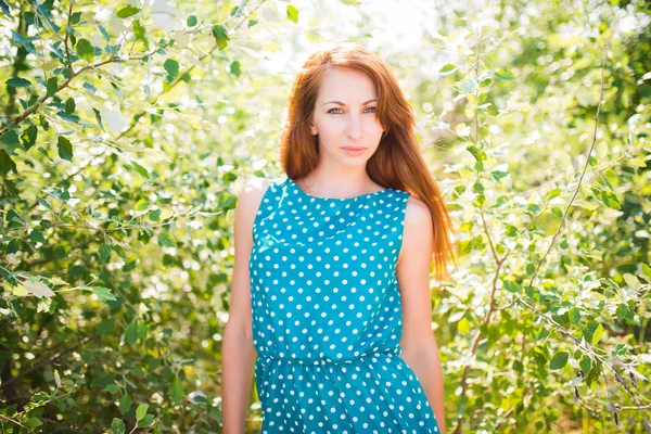 Young woman in dress standing with blooming trees at background — 스톡 사진