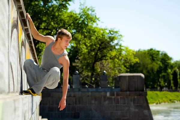 Young man in sportswear practicing parkour outside on stone wall on clear summer day — Stock Photo, Image