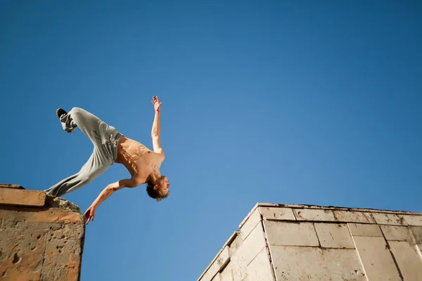 Young man jumping and practicing parkour between two building outside on clear summer day — ストック写真