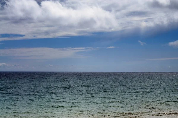 Wybrzeże morskie i skalista plaża, błękitne zachmurzone niebo — Zdjęcie stockowe