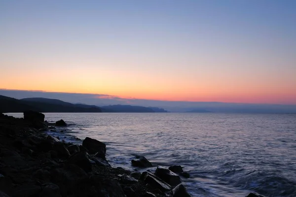 Pôr do sol junto ao mar, praia repleta de pedras — Fotografia de Stock