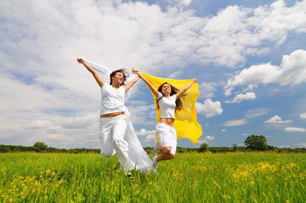 Young happy women jumping and holding silk shawls in meadow — Stock Photo, Image
