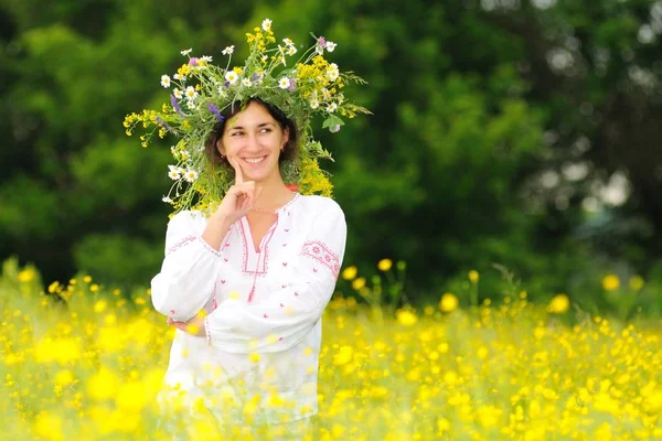 Mujer sonriente en ropa nacional y corona de flores de pie en el prado — Foto de Stock